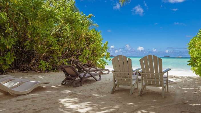 Zwei Holzstühle sitzen auf einem sandigen Strand
