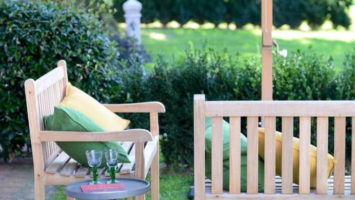 Eine Bank mit grünen Kissen und gelben Kissen neben einem Tisch mit zwei Gläsern und einem Buch