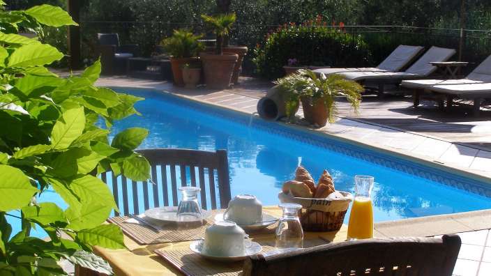 Ein Tisch mit einem Korb Brot und Orangensaft neben einem Swimmingpool