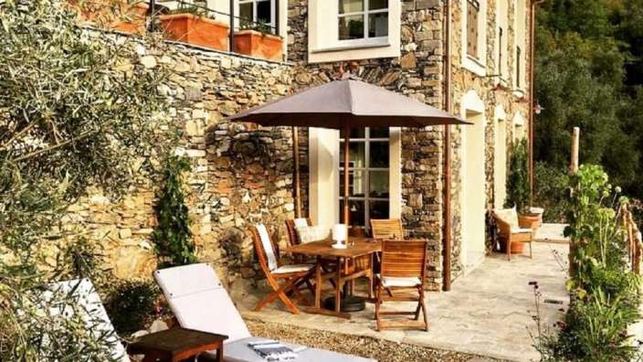 Eine Terrasse mit einem Tisch und Stühlen und einem Regenschirm vor einem Steingebäude