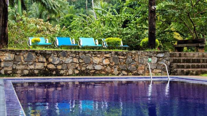 Ein Pool mit blauen Stühlen und einer Steinmauer im Hintergrund