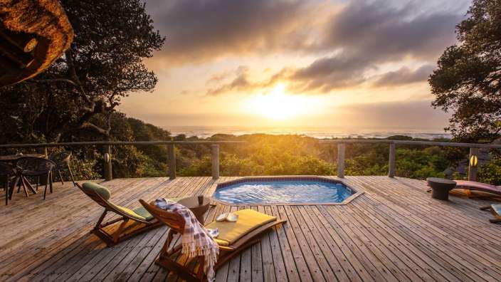 Ein Holzdeck mit einem Pool und Liegestühlen und einem Sonnenuntergang im Hintergrund