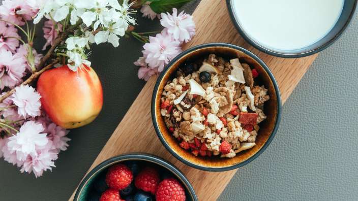 Drei Schüsseln mit Müsli und Früchten auf einem Holzbrett