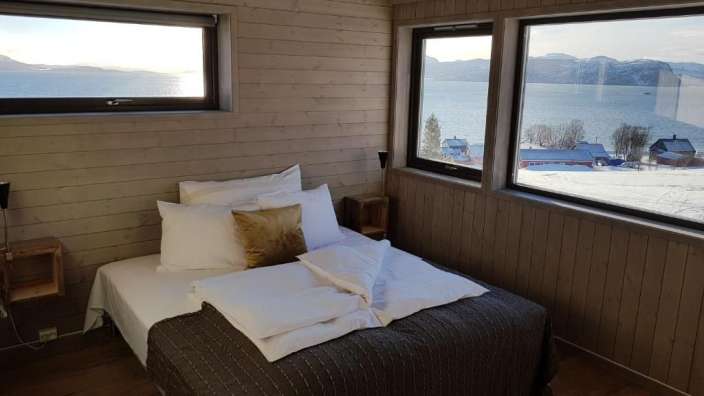 Ein Schlafzimmer mit einem Bett und zwei Fenstern mit Blick auf einen See