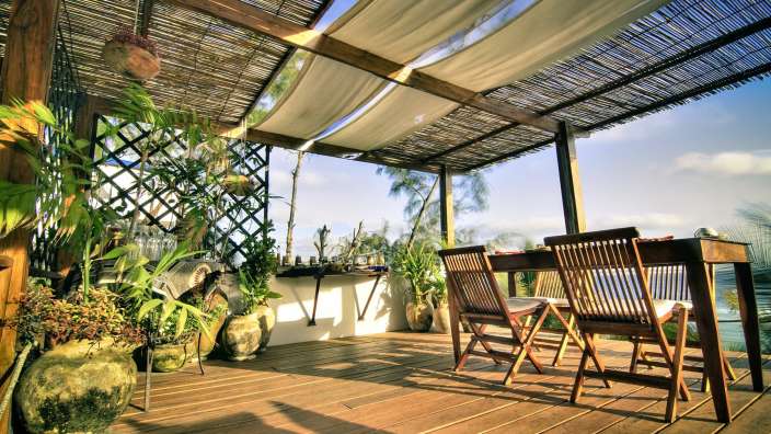 Ein Holzdeck mit einem Tisch und Stühlen unter einem Strohdach