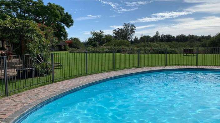 Ein großer Swimmingpool mit einem Zaun umgeben von Gras und Bäumen