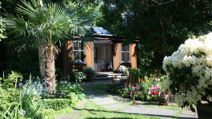 Ein kleines Haus in einem Garten mit Palmen und Blumen