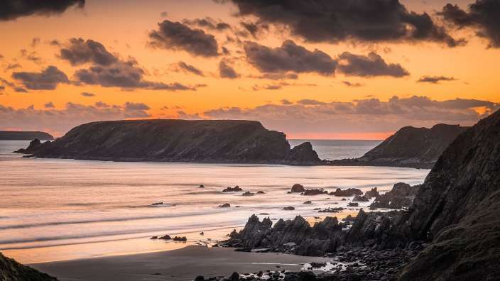 Ein Sonnenuntergang über einem felsigen Strand mit einem großen Felsen im Hintergrund