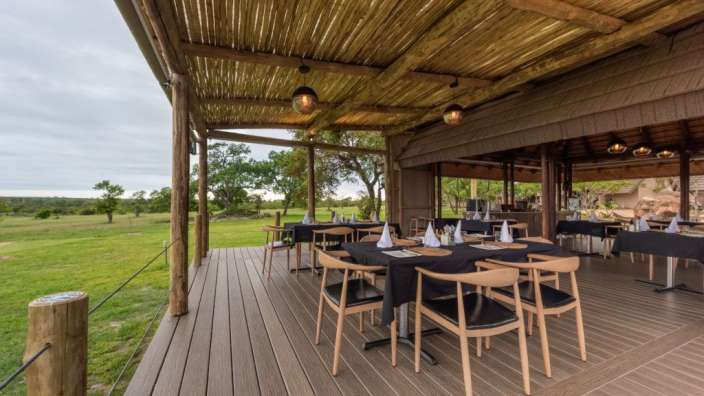 Tische und Stühle auf einem Deck mit Blick auf eine Wiese