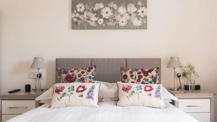 Ein Bett mit Blumenkissen und einem Gemälde an der Wand