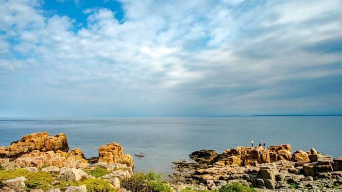 Menschen stehen auf einem Felsen über dem Ozean