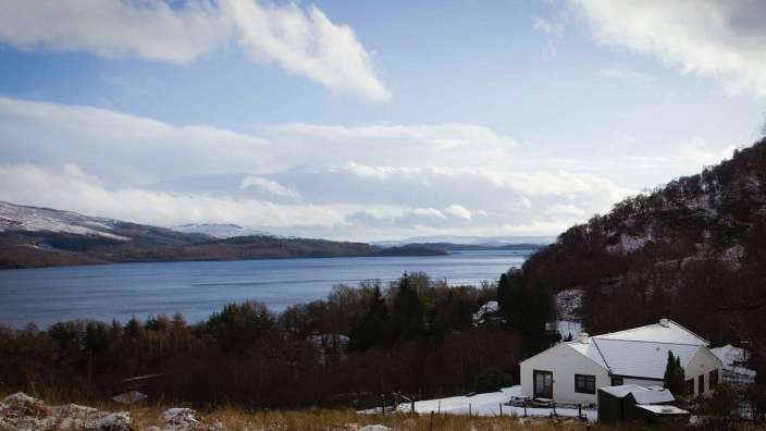 Ein weißes Haus steht auf einem schneebedeckten Hügel neben einem See