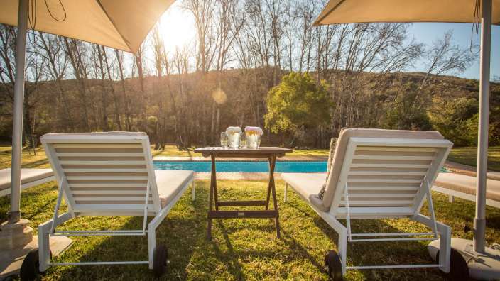 Liegestühle stehen neben einem Tisch mit Gläsern und Wasserkannen in der Nähe eines Swimmingpools