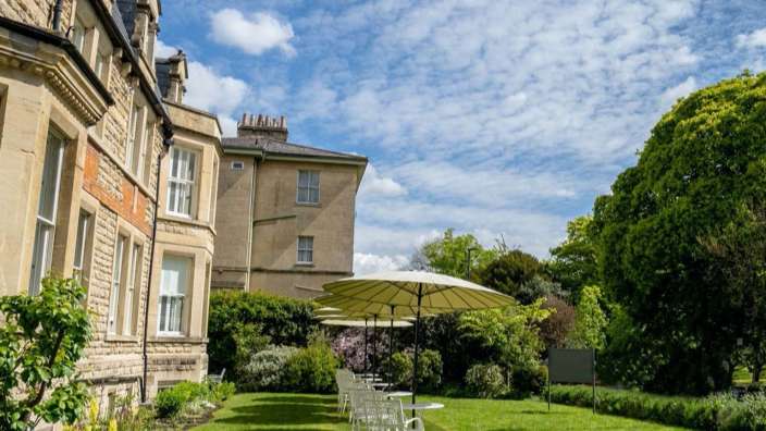 Eine Reihe von Tisch und Stühlen mit Sonnenschirmen vor einem großen Gebäude