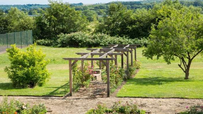 Ein Garten mit einer Holzpergola und Blumenbeet