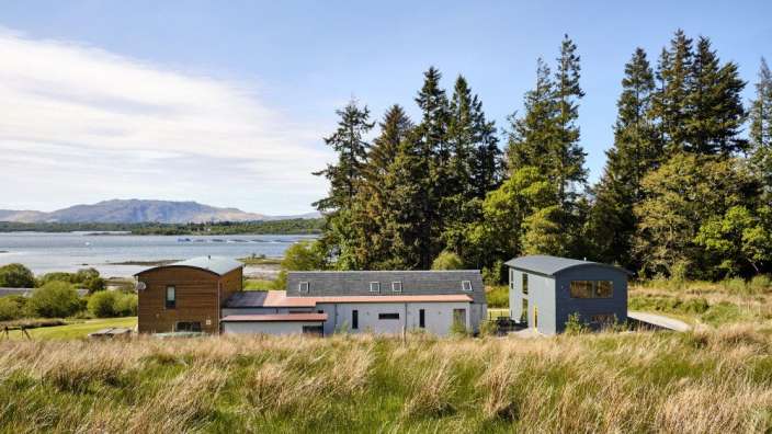 Drei Häuser stehen auf einer Wiese mit Blick auf einen See