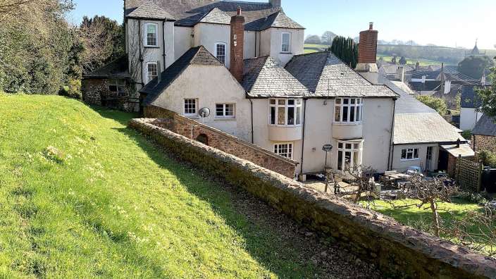 Ein großes Haus auf einem Hügel mit einer Steinmauer davor