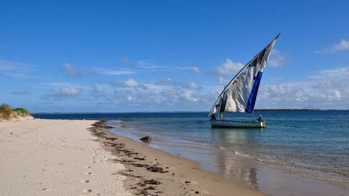 Ein Boot mit einem blauen und weißen Segel schwimmt am Strand