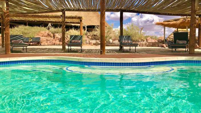 Ein Swimmingpool mit Liegestühlen und einem Strohdach darüber