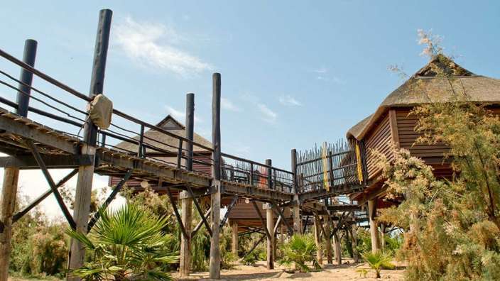 Eine Brücke führt zu einem Holzhaus mit Strohdach