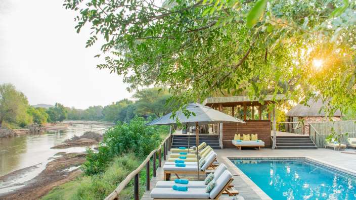 Ein Swimmingpool mit Liegestühlen und Sonnenschirmen neben einem Fluss