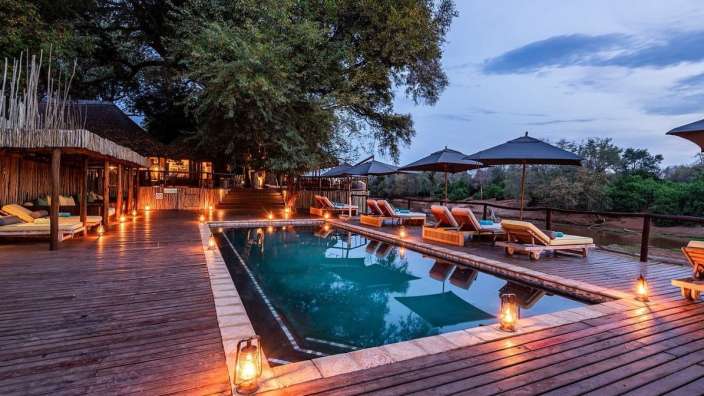 Ein großer Swimmingpool auf einem Holzdeck mit Sonnenliegen und Regenschirmen