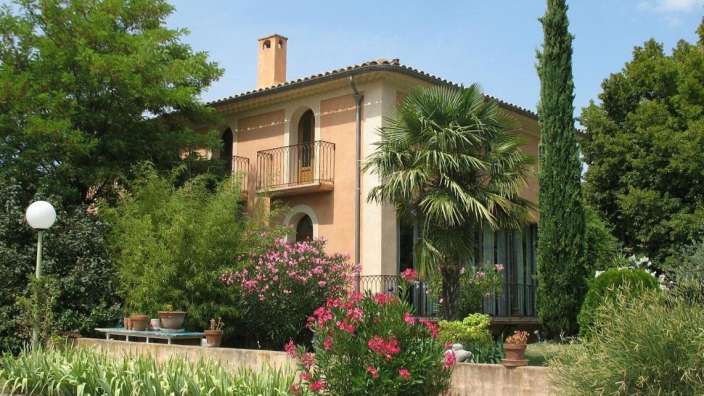 Ein großes Haus mit einem Balkon und Palmen davor