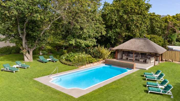 Ein großer Swimmingpool in einem Garten mit Liegestühlen und einem Strohpavillon