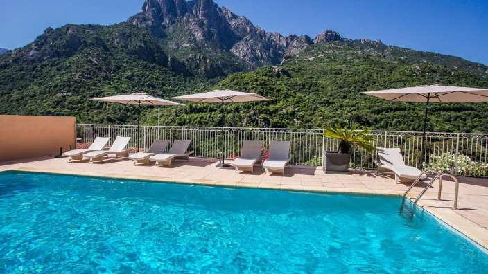 Ein Swimmingpool mit Liegestühlen und Sonnenschirmen und einem Berg im Hintergrund