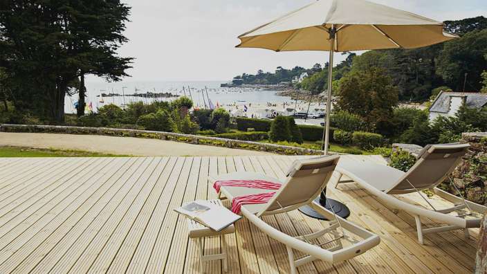 Ein Deck mit Liegestühlen und einem Sonnenschirm mit Blick auf das Meer