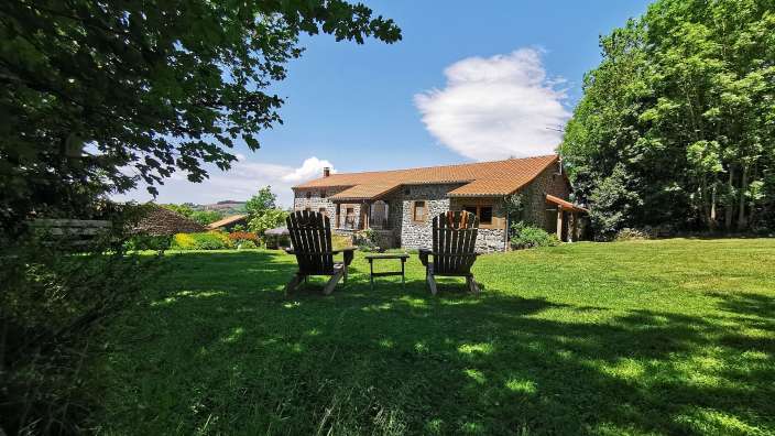 Zwei Holzstühle sitzen auf einem grünen Rasen vor einem Steinhaus