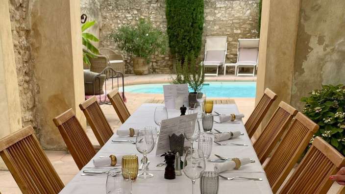 Ein langer Tisch mit Holzstühlen und Gläsern steht vor einem Pool