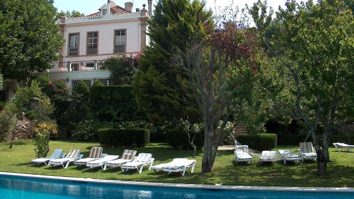 Liegestühle um einen Pool mit einem großen Haus im Hintergrund