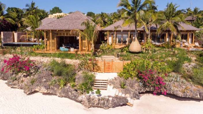 Ein großes Holzhaus mit Strohdach sitzt auf einem Sandstrand