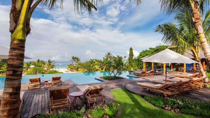 Liegestühle und Sonnenschirme rund um einen Pool mit Blick auf das Meer