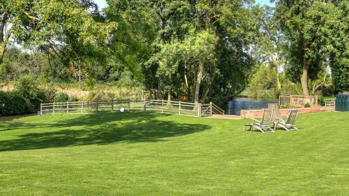 Ein grüner Rasen mit Stühlen und einem Holzzaun