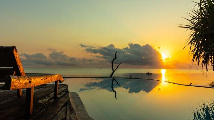 Die Sonne geht über dem Ozean unter und spiegelt sich im Pool