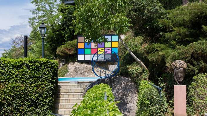 Ein buntes Quadrat steht in einem Garten neben einer Statue