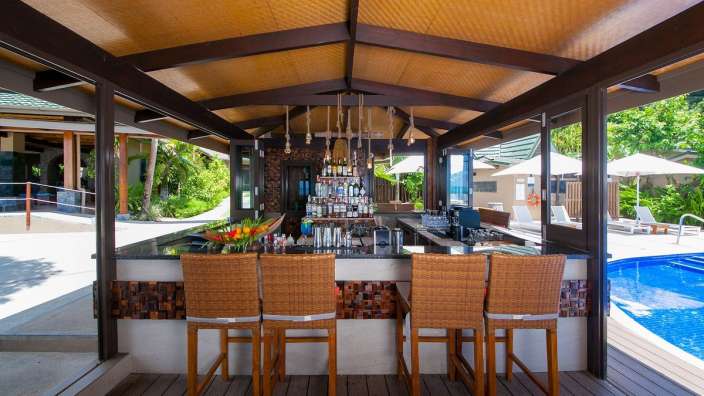 Eine Bar mit Stühlen und Flaschen an der Spitze neben einem Pool