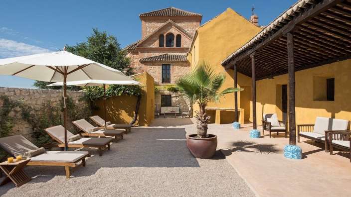 Eine Terrasse mit Liegestühlen und Sonnenschirmen vor einem gelben Gebäude