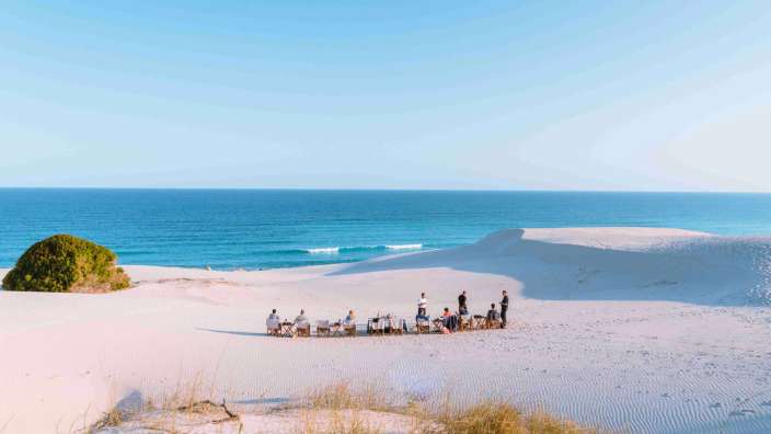 Eine Gruppe von Menschen sitzt auf einer Düne mit Blick auf das Meer
