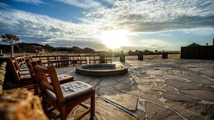 Die Sonne scheint über einen Steinplatz mit Stühlen und einem Feuer