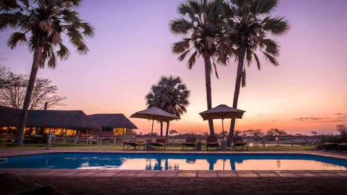 Ein Swimmingpool mit Palmen und Sonnenuntergang im Hintergrund