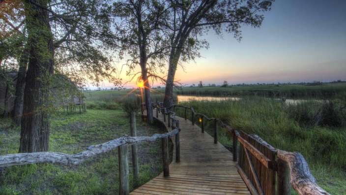 Ein Holzsteg führt zu einem Teich bei Sonnenuntergang