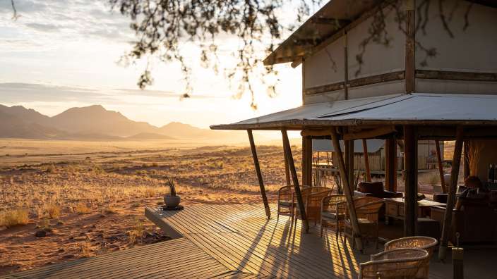 Ein Holzdeck mit Stühlen und einem Tisch vor einem Haus in der Wüste