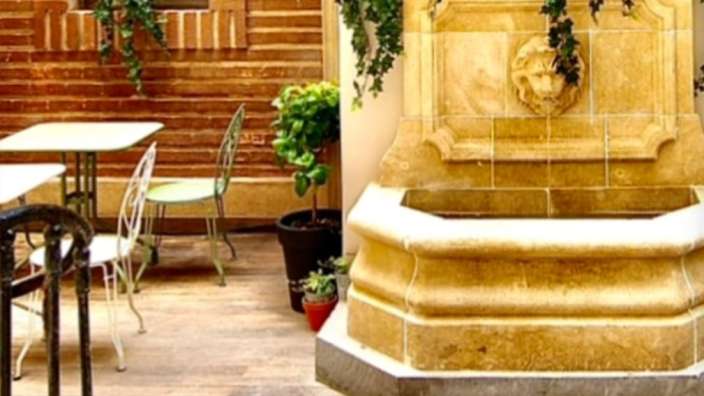 Ein Brunnen mit einem Löwenkopf darauf steht neben einem Tisch und Stühlen