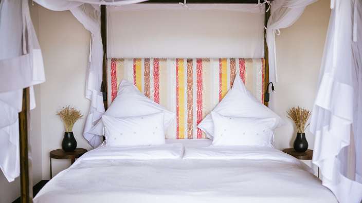 Ein Himmelbett mit weißen Bettwäschen und einem bunten Kopfteil