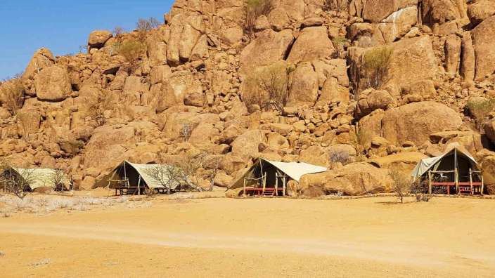 Drei Zelte stehen in der Wüste vor einem Felsen