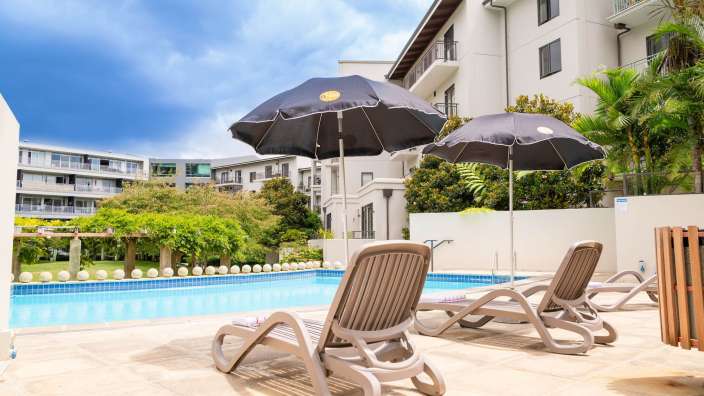 Liegestühle und Sonnenschirme neben einem Pool mit einem Gebäude im Hintergrund