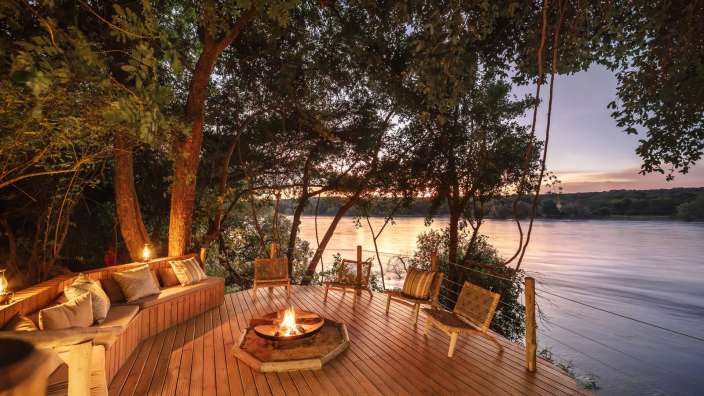 Ein Holzdeck mit einem Feuer und Stühlen über einem Fluss